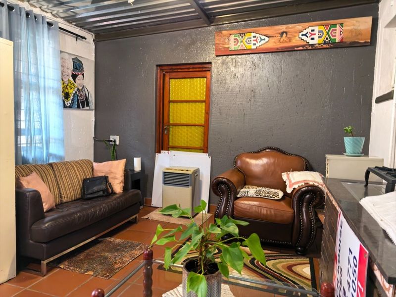Living room featuring terracotta floor tiles, a corrugated metal ceiling, and a timber-framed door with textured glass panels.