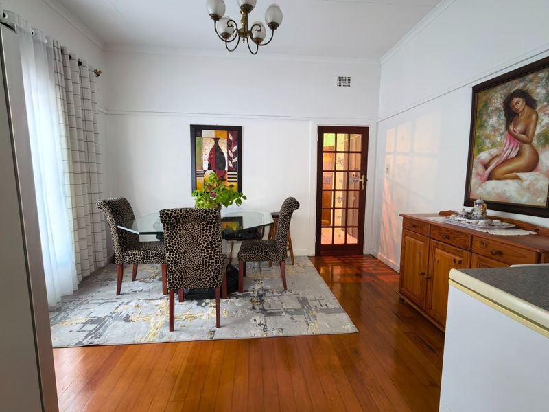 A well-maintained dining room featuring polished hardwood flooring, a classic timber-framed glass door, and traditional picture rails.