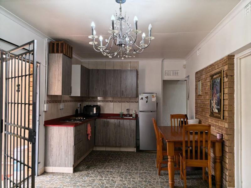 Open plan kitchen and dining area featuring wood-look cabinetry, red laminate countertops, an exposed brick wall, and decorative chandelier lighting.