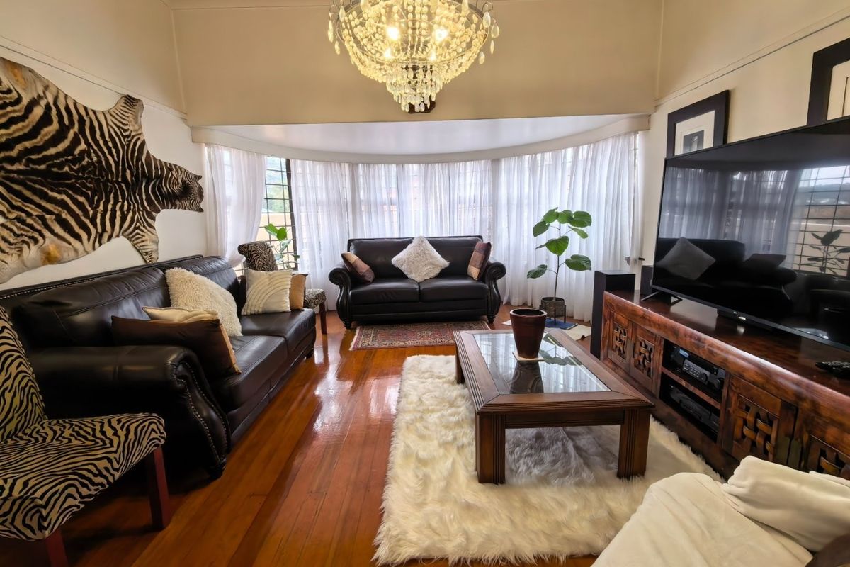A well-maintained living room featuring polished hardwood flooring, a large bay window with natural light, and an elegant crystal chandelier.