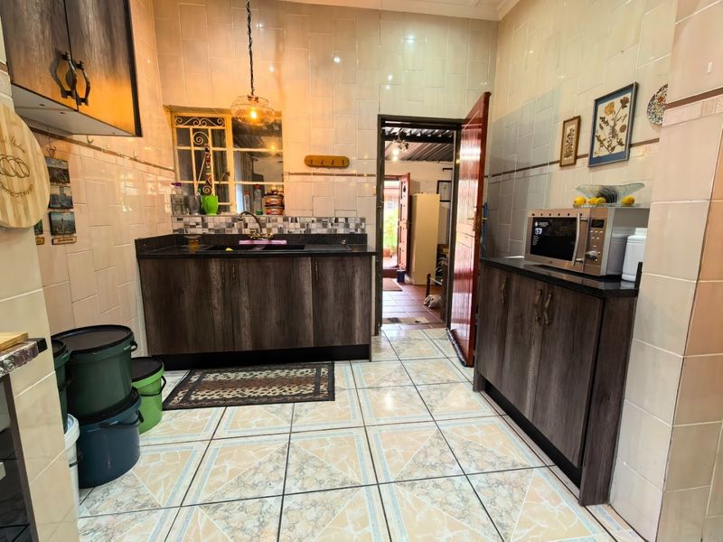 A functional kitchen featuring dark wood-look cabinetry, granite countertops, tiled walls, and tiled flooring, providing a practical workspace with direct access to the rear.