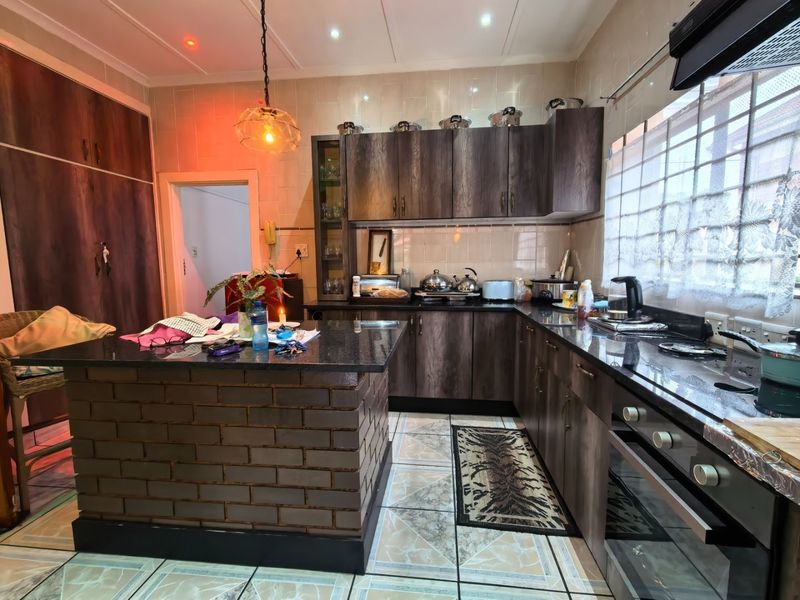 A functional kitchen featuring dark wood cabinetry, granite countertops, a unique brick-base island, and tiled finishes throughout.