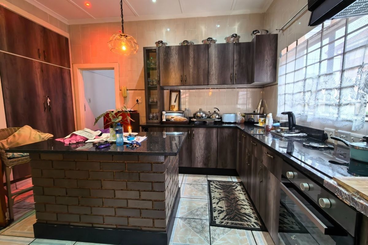 A functional kitchen featuring dark wood cabinetry, granite countertops, a unique brick-base island, and tiled finishes throughout.