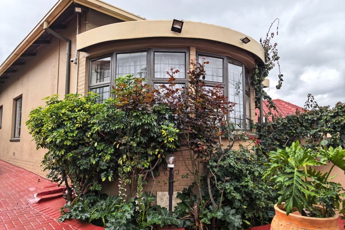 A view of the rear exterior featuring a distinctive curved bay window, brick paved patio area, and established garden landscaping.