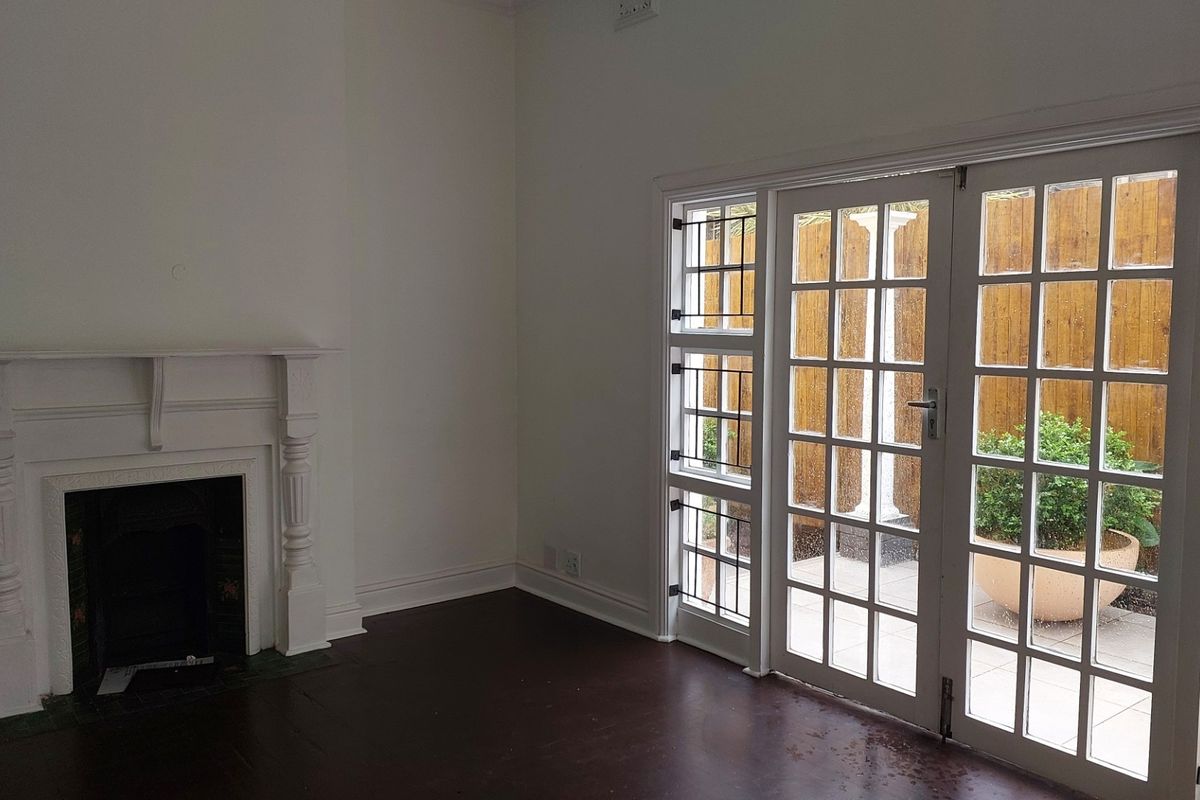 An empty living room featuring a classic fireplace mantel, dark timber flooring, and glass-paned french doors providing access to an outdoor patio area.