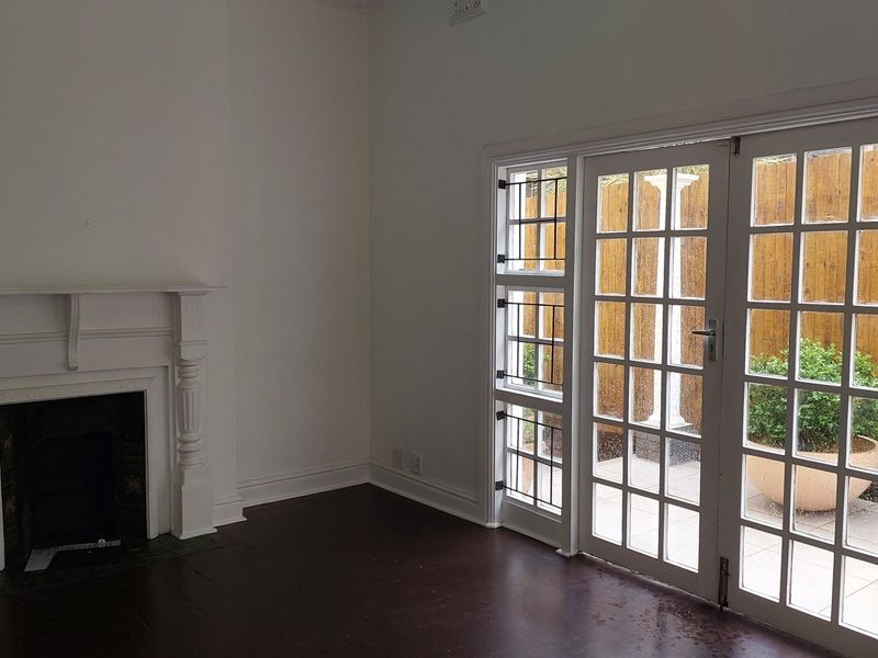 An empty living room featuring a classic fireplace mantel, dark timber flooring, and glass-paned french doors providing access to an outdoor patio area.