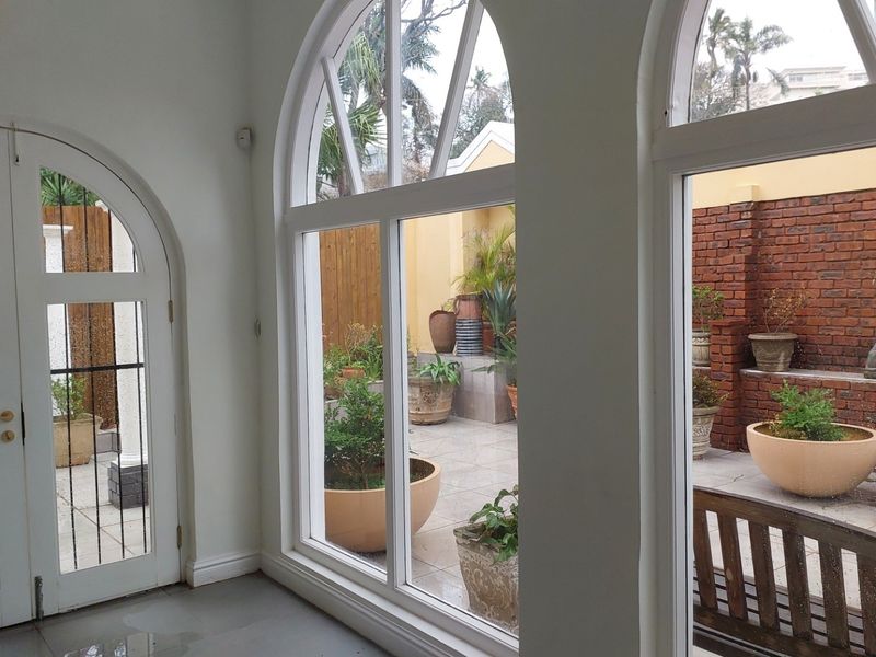 Bright office space featuring large arched windows and double doors providing direct access to a private paved courtyard area.