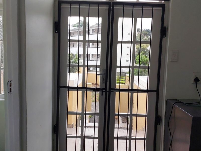 An interior view of an entry area featuring white french doors with a black security gate, providing access to an outdoor space.