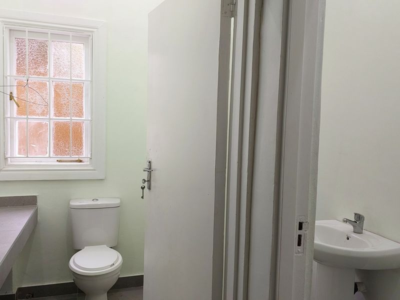 A functional bathroom featuring a pedestal basin, a toilet, and a built-in vanity counter, illuminated by a window with security bars.