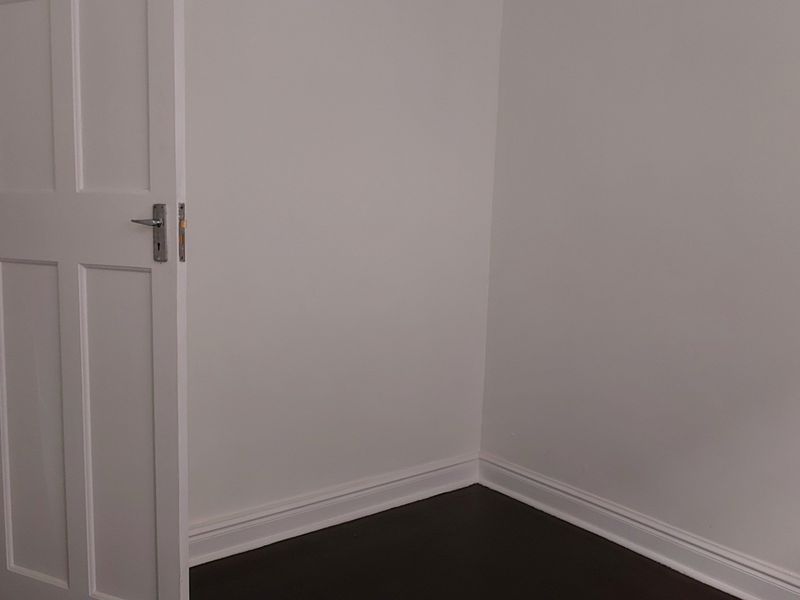 An empty office space featuring dark flooring, white walls, and a view into an adjacent bathroom.