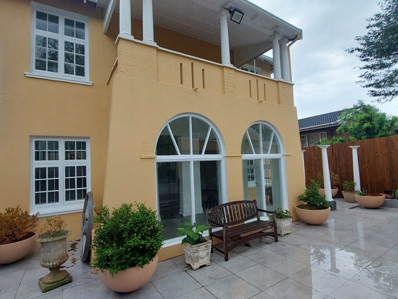 Rear view of the office building featuring a paved patio area, arched windows, and an upper-level balcony with classic architectural columns.