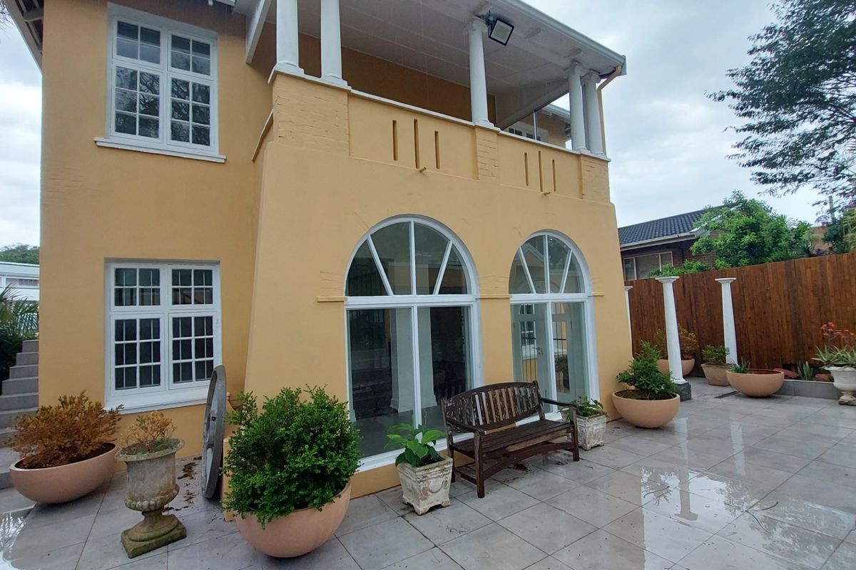 Rear view of the office building featuring a paved patio area, arched windows, and an upper-level balcony with classic architectural columns.