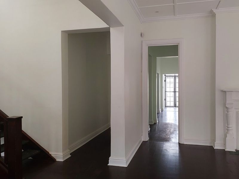 Spacious hallway featuring dark hardwood flooring, a classic fireplace mantel, and a wooden staircase, leading through to a secure rear entrance.