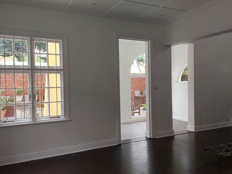 A bright, vacant office space featuring polished timber flooring, classic architectural mouldings, and large multi-pane windows overlooking an outdoor courtyard area.