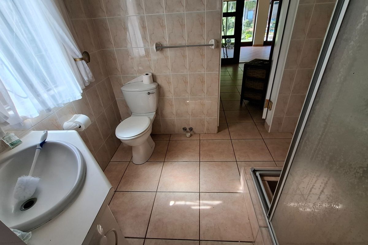 A functional bathroom featuring a vanity basin, toilet, and shower enclosure with neutral wall and floor tiling.