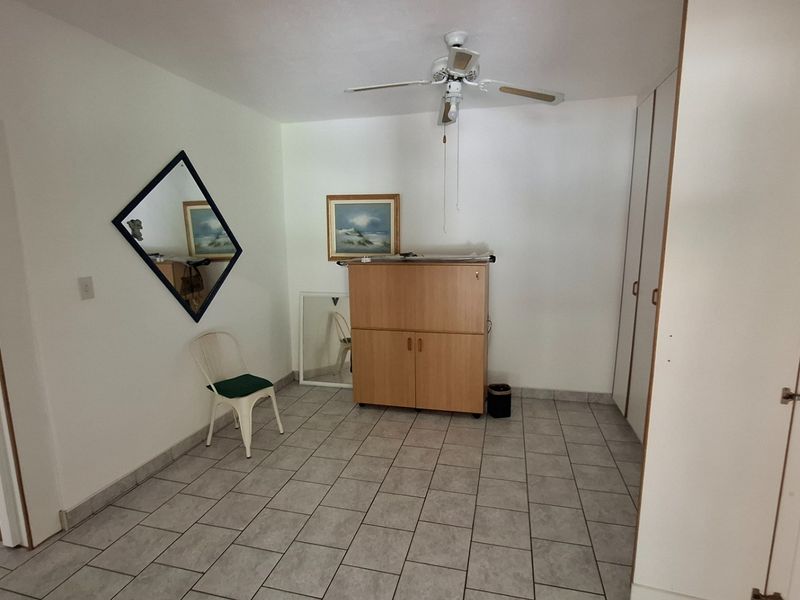A bedroom featuring tiled flooring, a ceiling fan, and built-in cupboards, offering a functional space ready for personalization.