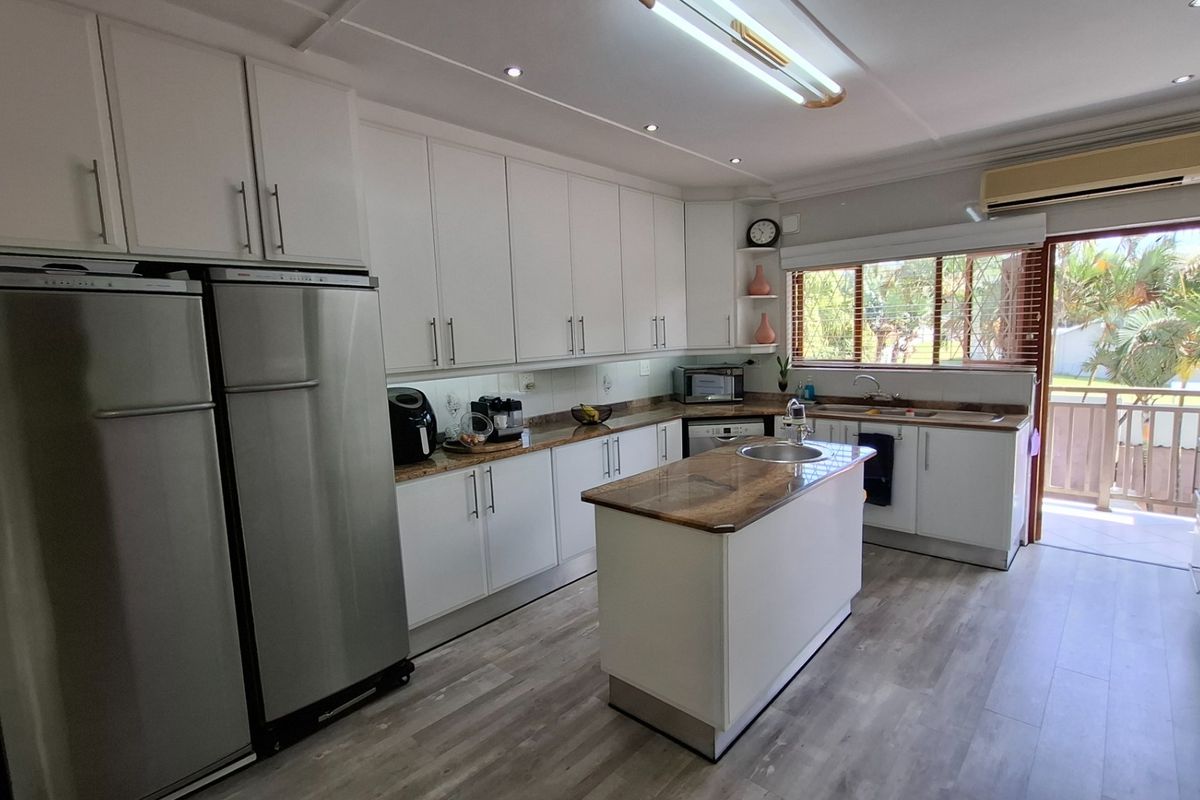 Modern kitchen featuring white cabinetry, stone countertops, a central island with a sink, and direct access to an outdoor patio area.
