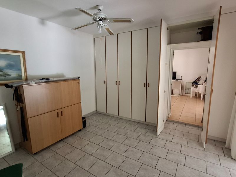 A bedroom featuring built-in cupboards, a ceiling fan, and tiled flooring, with an adjoining room visible through the doorway.