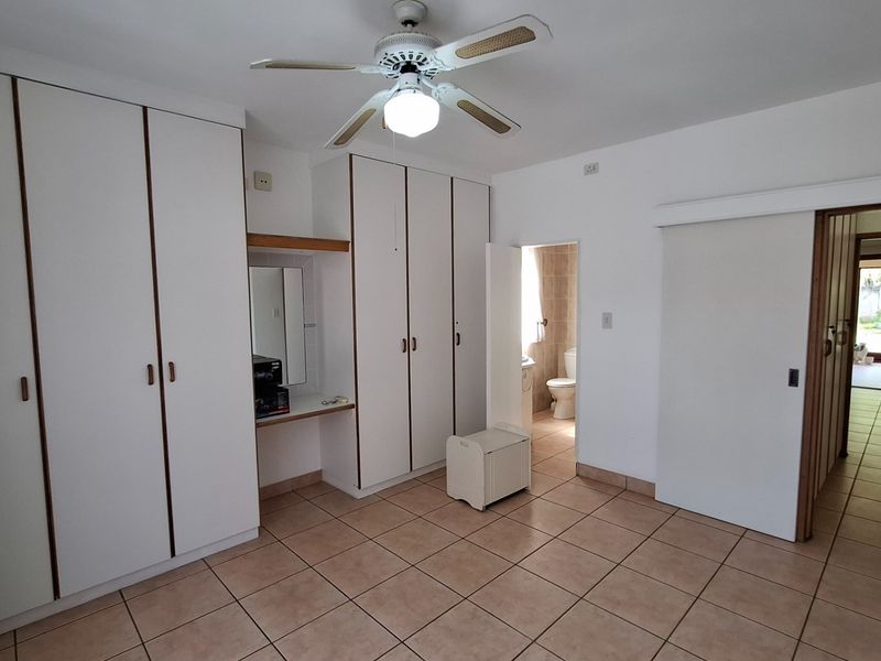 Spacious bedroom featuring extensive built-in cupboards, a ceiling fan, tiled flooring, and direct access to an en-suite bathroom.