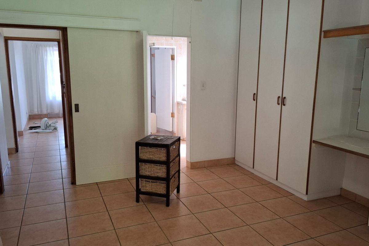 A spacious bedroom featuring built-in cupboards, a vanity area, and tiled flooring, with direct access to an adjoining hallway and bathroom.