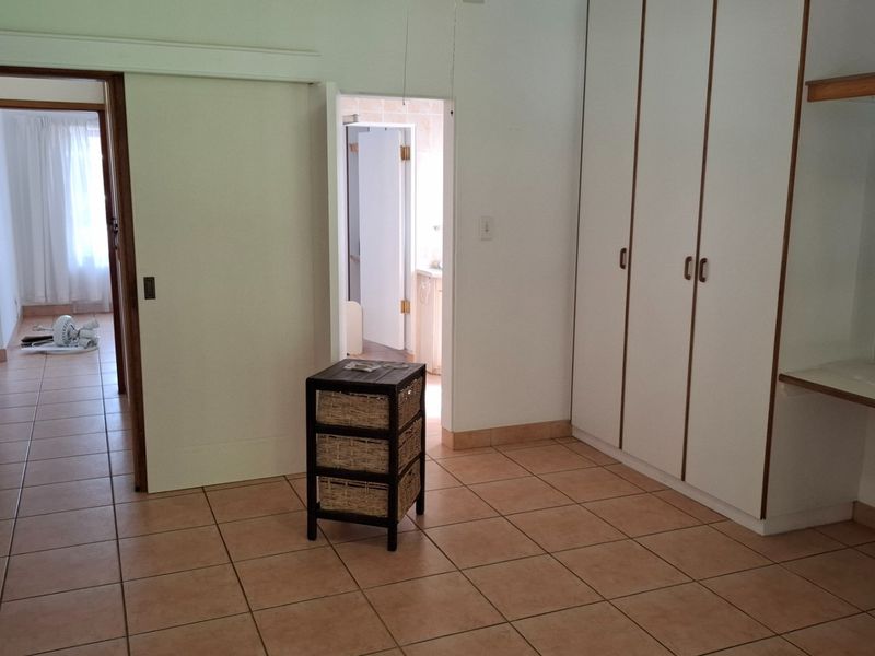 A spacious bedroom featuring built-in cupboards, a vanity area, and tiled flooring, with direct access to an adjoining hallway and bathroom.