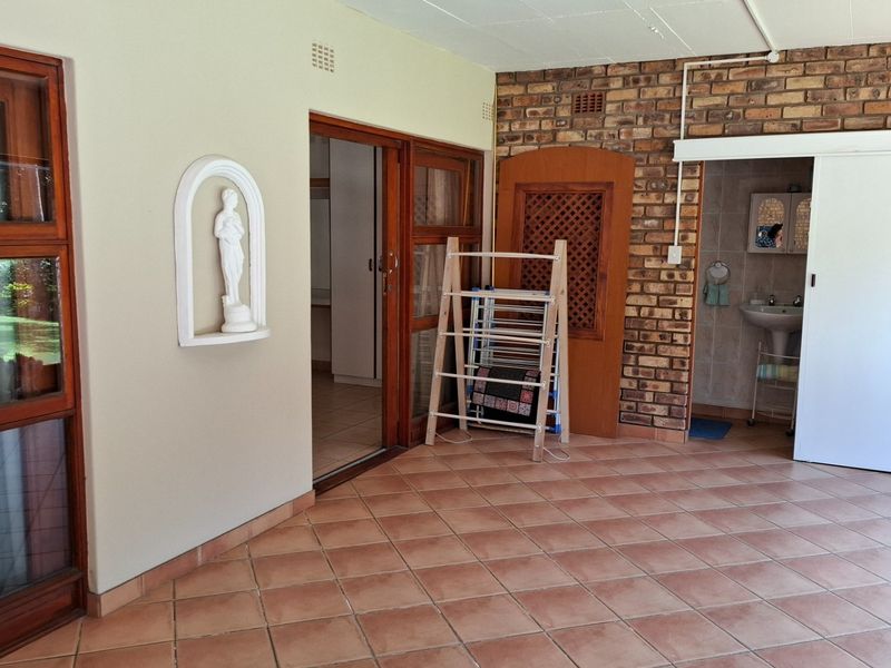 A covered patio area featuring terracotta tiling, exposed brickwork, and direct access to an adjoining bathroom with a pedestal basin.