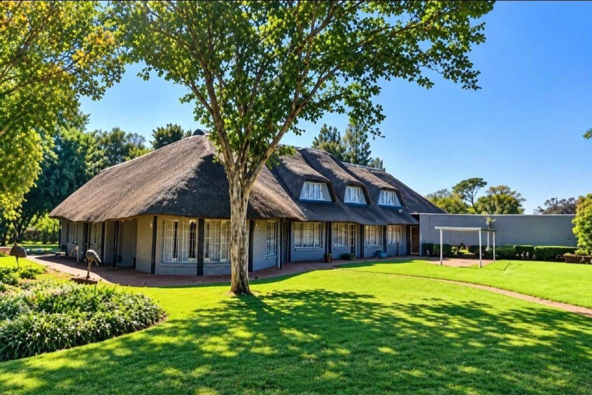 A well-maintained small holding property featuring a traditional thatched roof, dormer windows, and expansive landscaped gardens.