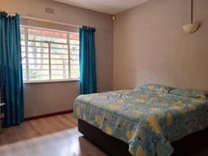A standard bedroom featuring laminate flooring, large windows with security bars, and a wall-mounted light fixture.