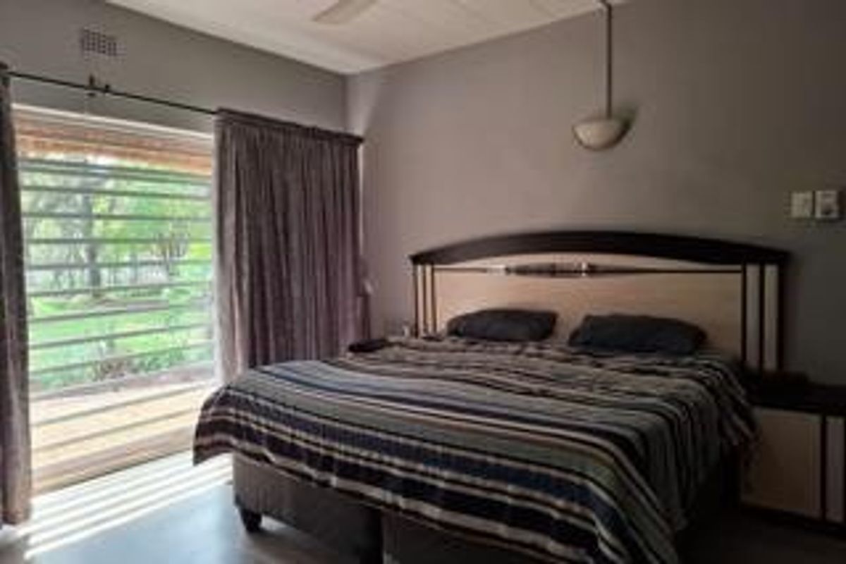 A bedroom featuring a ceiling fan, wall-mounted lighting, and a sliding glass door with a security gate providing access to the outdoors.
