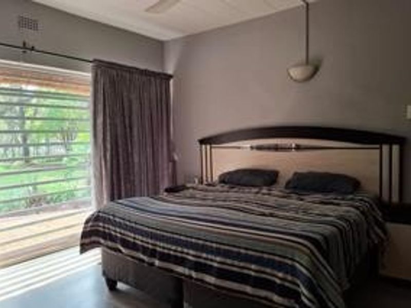 A bedroom featuring a ceiling fan, wall-mounted lighting, and a sliding glass door with a security gate providing access to the outdoors.