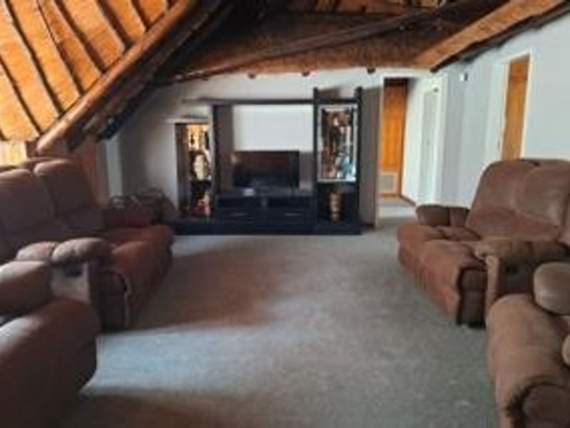 Spacious living room featuring a high-pitched exposed thatch roof with timber trusses, creating a rustic and airy atmosphere.