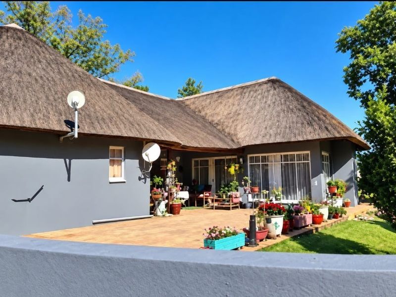 Rear view of a small holding property featuring a traditional thatched roof, a spacious paved patio area, and large sliding glass doors.