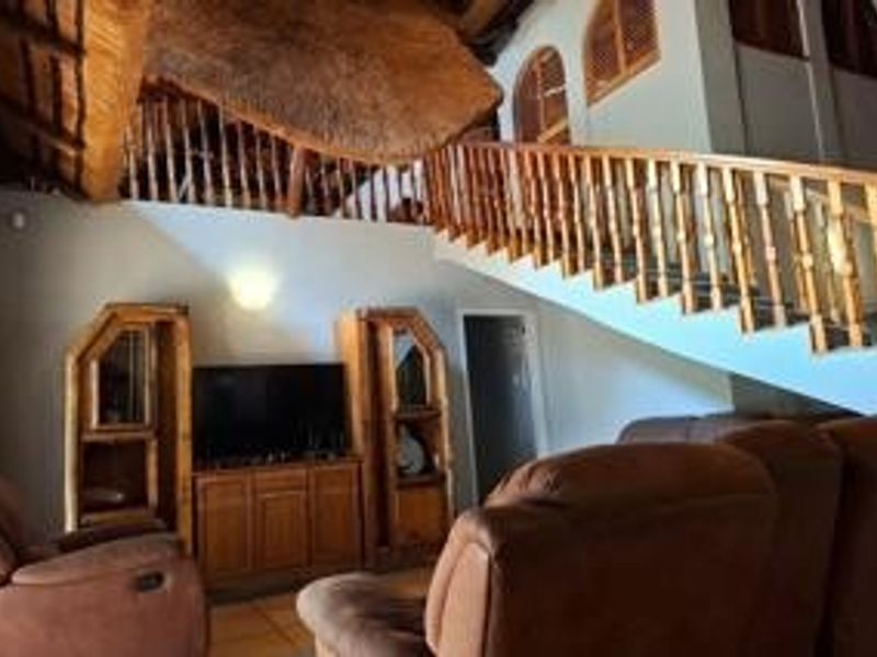 Spacious living area featuring a high thatch roof with exposed timber rafters and a prominent wooden staircase with a matching balustrade.