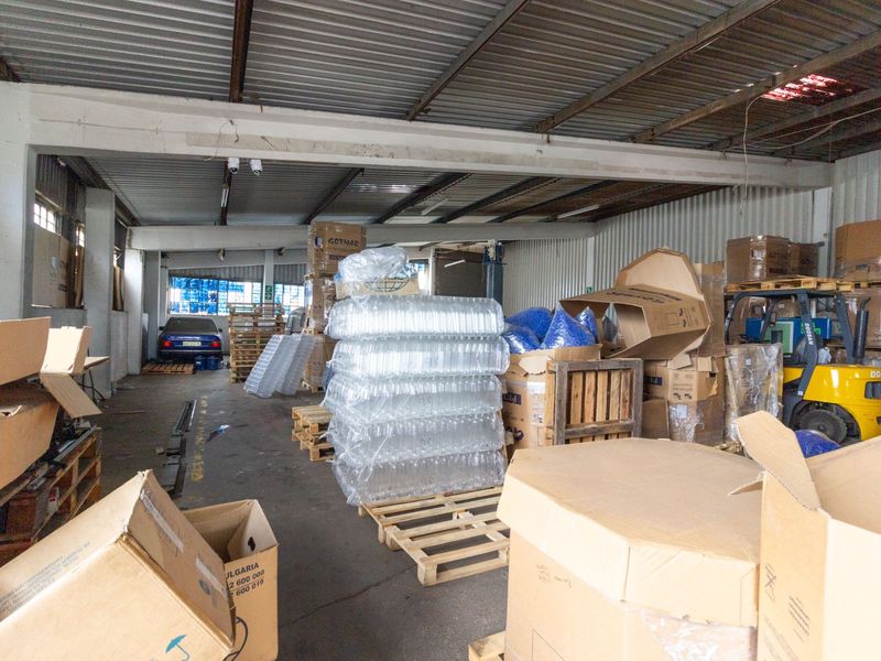 Industrial warehouse space featuring high ceilings with exposed steel beams, corrugated metal roofing, and durable concrete flooring, currently utilized for storage.