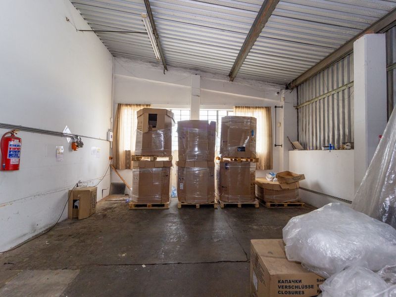 Industrial utility space featuring exposed metal roofing, concrete flooring, and wall-mounted fire safety equipment, suitable for storage or workshop use.