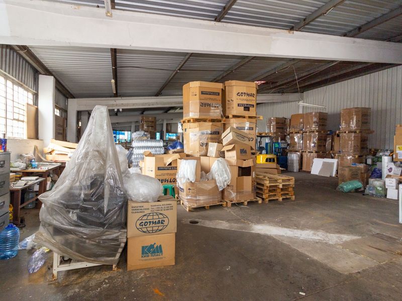 Spacious industrial utility area featuring exposed steel roof structure, concrete flooring, and large industrial windows, currently utilized for storage and operational purposes.