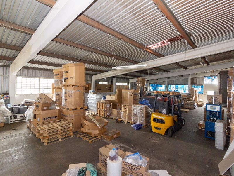 Spacious industrial warehouse area featuring exposed steel beams, corrugated metal roofing, and concrete flooring, suitable for storage or manufacturing operations.