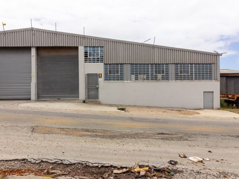 Industrial warehouse exterior featuring dual roller shutter doors, steel security access, and corrugated metal cladding with perimeter electric fencing.