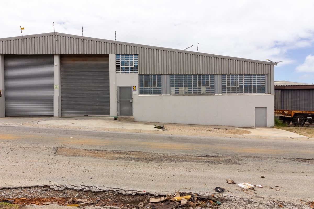 Industrial warehouse exterior featuring dual roller shutter doors, steel security access, and corrugated metal cladding with perimeter electric fencing.