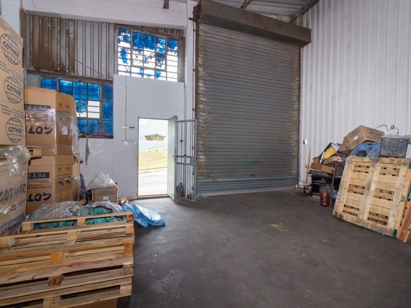 Industrial warehouse space featuring a large roller shutter door, high ceilings, and secure access, suitable for storage or light manufacturing operations.