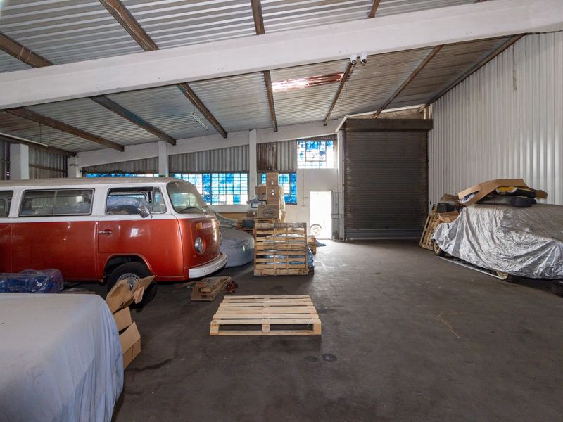 Spacious industrial utility area featuring high ceilings, exposed steel beams, metal wall cladding, and a large roller shutter door for easy access.