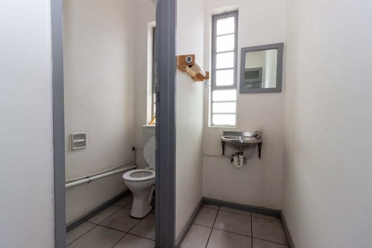 A functional industrial-style bathroom featuring a toilet, stainless steel basin, tiled flooring, and a window for natural light.