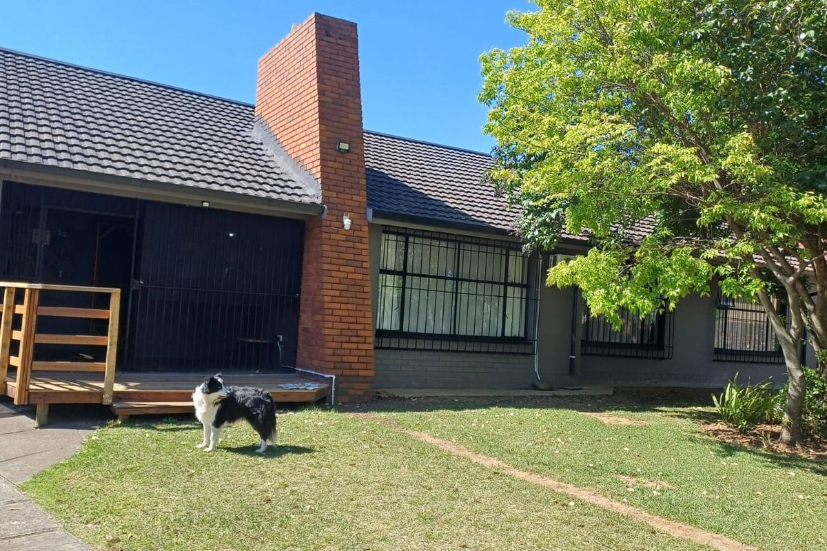Rear view of the house featuring a brick chimney, tiled roof, security bars on windows, and a wooden deck leading to the garden.