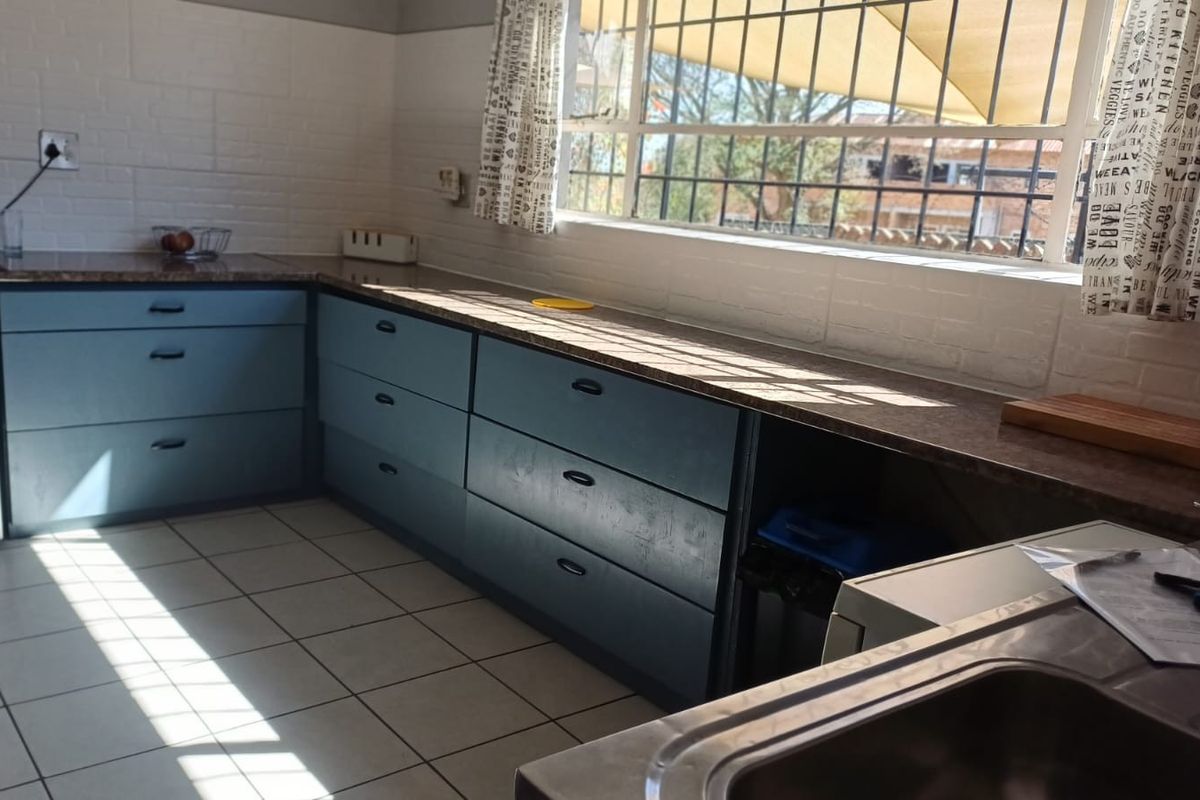 A functional kitchen featuring blue cabinetry, laminate countertops, ceramic floor tiling, and a stainless steel sink with natural light from the window.