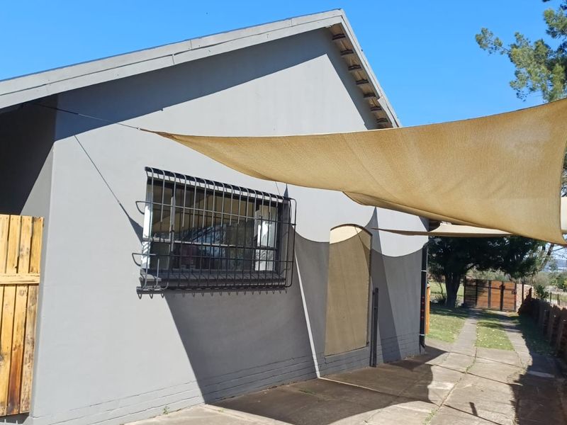 Rear exterior view of the property featuring a paved walkway, security bars on the window, and a shade sail for outdoor coverage.