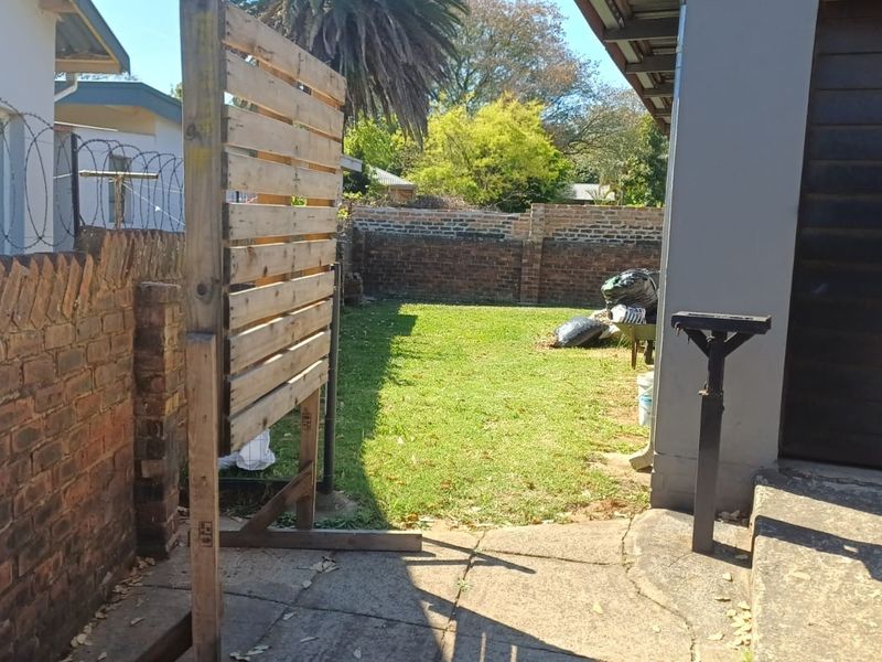 A rear garden area featuring a lawn, concrete paving, and brick boundary walls with security razor wire.