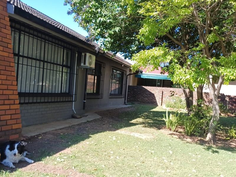 A view of the rear exterior of the house featuring a brick facade, security bars on windows, and a private garden area.