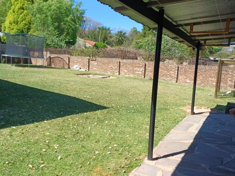 A covered patio area with stone paving overlooking a spacious backyard with a brick boundary wall and water storage tank.