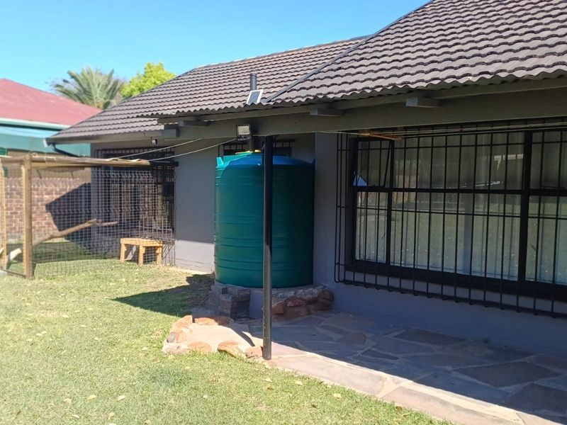 Rear exterior view of the house featuring a paved patio area, security bars on windows, and a large water storage tank.