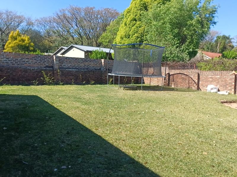 A spacious backyard featuring a well-maintained lawn enclosed by a traditional brick boundary wall.